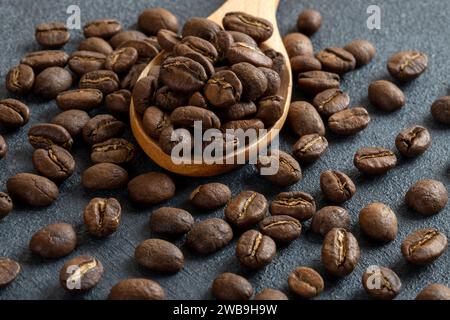 Un cucchiaio pieno di chicchi di caffè tostati su sfondo nero Foto Stock
