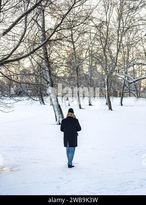 Un uomo che passeggia davanti a una panchina in un parco innevato a Helsinki, Finlandia, in inverno Foto Stock