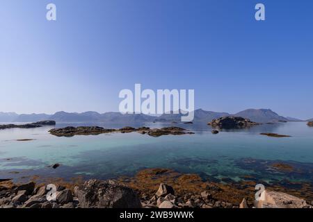 Le acque cristalline incontrano le rive rocciose del Lofoten, offrendo una vista tranquilla delle montagne lontane sotto la vasta distesa del cielo nordico Foto Stock