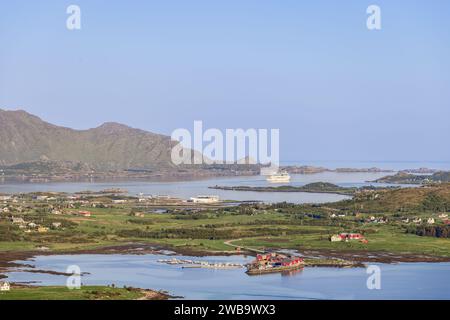 L'ora d'oro proietta un caldo bagliore su un fiordo norvegese, dove una nave da crociera riposa tra isole sparse, con le tradizionali cabine rorbuer Foto Stock