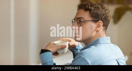 Tranquillo studente europeo millenario in bicchieri beve tè, gusta una tazza di caffè Foto Stock