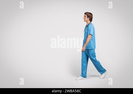 Medico maschile in scrub camminare, vista laterale Foto Stock
