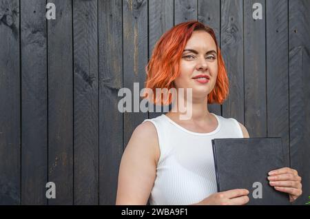 Donna rossa con tavoletta di registrazione su sfondo nero in legno Foto Stock