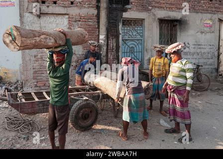 I portatori trasportano tronchi pesanti sulle rive del fiume Buriganga a Dacca in Bangladesh Foto Stock