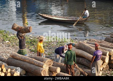 I portatori trasportano tronchi pesanti sulle rive del fiume Buriganga a Dacca in Bangladesh Foto Stock