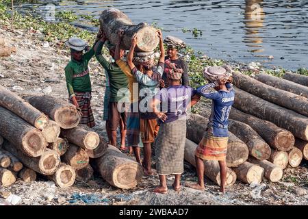 I portatori trasportano tronchi pesanti sulle rive del fiume Buriganga a Dacca in Bangladesh Foto Stock