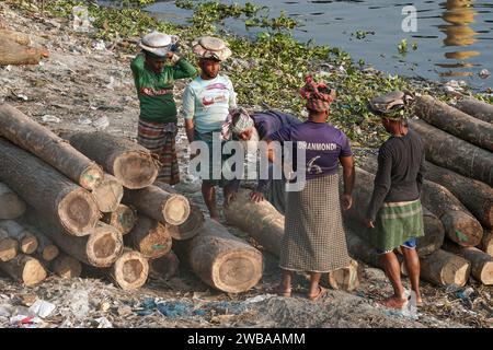 I portatori trasportano tronchi pesanti sulle rive del fiume Buriganga a Dacca in Bangladesh Foto Stock