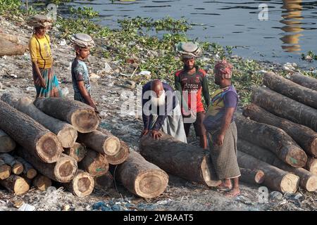 I portatori trasportano tronchi pesanti sulle rive del fiume Buriganga a Dacca in Bangladesh Foto Stock