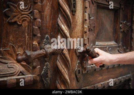 Mans hand is opening an ornate and beautifully wooden carved door that opens to a church. Stock Photo