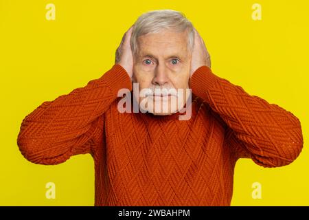 Non voglio sentire e ascoltare. Frustrato, infastidito, irritato, anziano anziano che copre le orecchie gestendo di no, evitando i consigli ignorando il rumore sgradevole e le voci forti. Nonno isolato su sfondo giallo Foto Stock