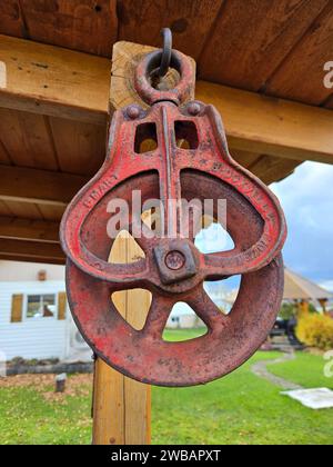 Un primo piano di un'antica puleggia attaccata a una trave di legno, con lussureggiante erba verde sullo sfondo Foto Stock