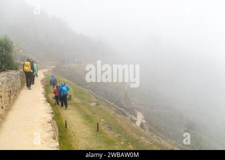 I turisti camminano attraverso le terrazze di un Machu Picchu nuvoloso in Perù Foto Stock