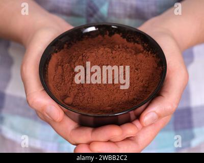 Una donna che tiene in mano una ciotola nera con polvere di cacao organico. Primo piano. Foto Stock