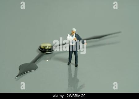 Fotografia di figure giocattolo in miniatura. Vai al concetto di lavoro. Un uomo d'affari che si prepara a indossare un vestito davanti alla Corth. Isolato su bac grigio Foto Stock