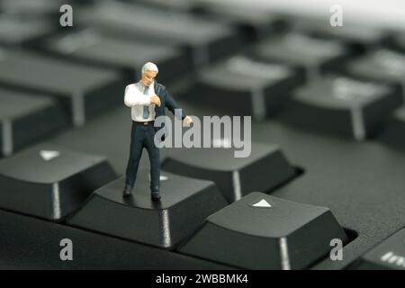 Fotografia di figure giocattolo in miniatura. Un uomo d'affari che si prepara a indossare un vestito sopra la tastiera. Isolato su sfondo bianco. ph. Immagine Foto Stock