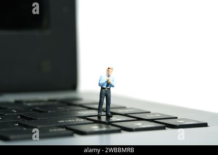 Fotografia di figure giocattolo in miniatura. Un uomo d'affari che si sta preparando, giustifica la cravatta sopra la tastiera del notebook. Isolato su sfondo bianco Foto Stock