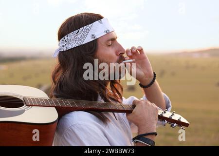 Elegante uomo hippie con fumante chitarra in campo Foto Stock