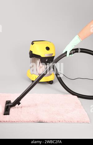 Donna tappeto hoovering su sfondo grigio Foto Stock