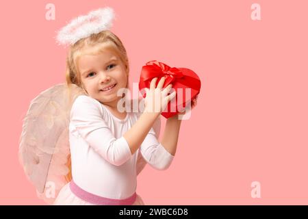 Graziosa bambina vestita da cupido con confezione regalo a forma di cuore su sfondo rosa. Festa di San Valentino Foto Stock