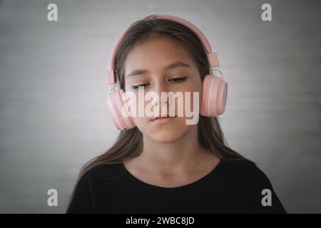 Una ragazza caucasica molto dispiaciuta che indossa un vestito nero arrabbiata indossa cuffie stereo per ascoltare la musica Foto Stock