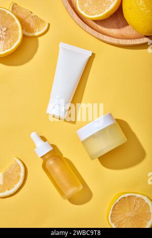 Sullo sfondo giallo, fette di limone fresche decorate con biberon per il mockup cosmetico - detergente per il viso, vaso panna e contagocce con ingredienti da Foto Stock