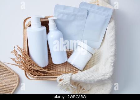 Vista dall'alto del set di prodotti per il bagno, bagno di sale e maschera di telo posta su cesto di bambù con asciugamano beige su sfondo bianco. Scena pubblicitaria Foto Stock