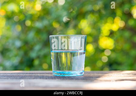 Vetro blu acqua su tavolo di legno con sfondo sfocato. Acqua pulita e pulita in un bicchiere Foto Stock