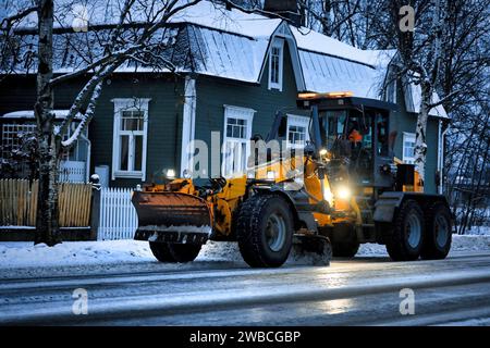 Motograder giallo Vammas RG 286 che rimuove la neve dalla strada la mattina presto dopo la nevicata invernale. Salo, Finlandia. 29 dicembre 2023. Foto Stock