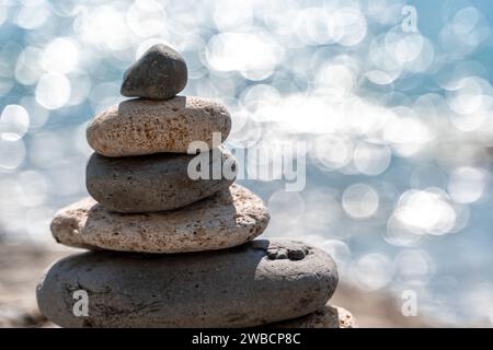 Torre di pietre. Una piramide di ciottoli bilanciata sulla spiaggia in una giornata di sole. Mare blu sullo sfondo. Messa a fuoco selettiva, bokeh. Pietre Zen sulla spiaggia di mare Foto Stock