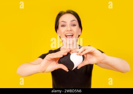 donna con t-shirt nera che regge il cuore bianco e balck come forma yin-yang su sfondo giallo. Persona romantica Foto Stock