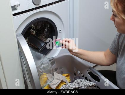Primo piano di una donna che mette una cialda di gel detergente in una lavatrice Foto Stock