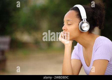 Profilo di una donna nera rilassata che indossa cuffie per ascoltare l'audio in un parco Foto Stock