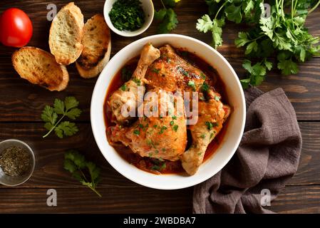 Stufato di pollo georgiano con pomodori ed erbe (chakhokhbili) in una ciotola su fondo di legno. Carne di pollo al forno con sugo di verdure al pomodoro. Sana e Foto Stock