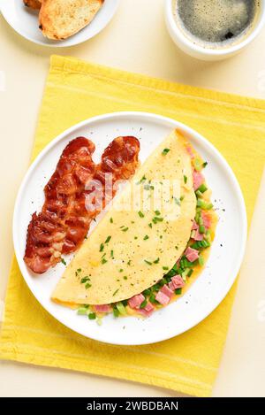 Omelette con prosciutto, cipolla verde, pancetta tostata e tazza di caffè su sfondo chiaro. Vista dall'alto, base piatta. Foto Stock