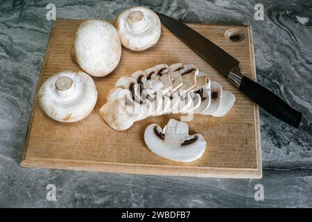 Vista dall'alto dei funghi champignon su un tagliere di faggio, uno dei quali è affettato ​​with un coltello Foto Stock