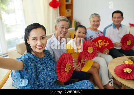 Donna sorridente che scatta selfie con i membri della famiglia quando festeggia Tet a casa Foto Stock