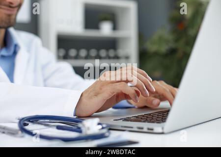 Stetoscopio e medico di base che utilizza un computer portatile alla scrivania in clinica che lavora su un computer Foto Stock