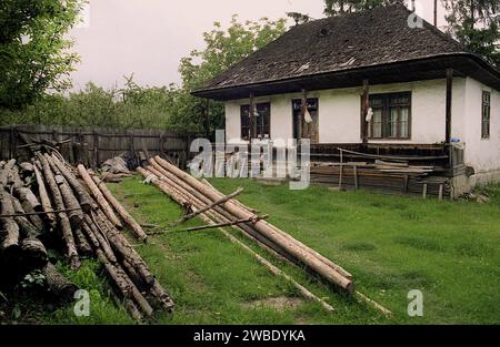Contea di Vrancea, Romania, circa 1995. Una casa tradizionale con tetto in legno in cattive condizioni. Legno impilato nel cortile. Foto Stock