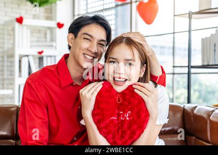 Una coppia felice che posa con i cuscini a forma di cuore nelle mani Foto Stock
