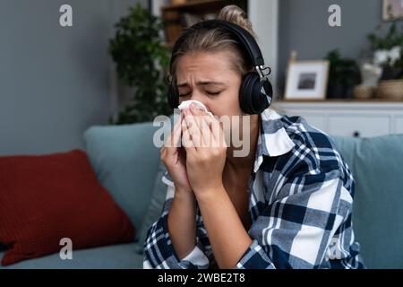 Giovane donna seduta a casa ad ascoltare audiolibri o podcast su cuffie wireless e a piangere. Si sente triste e depressa per il soggetto che hanno Foto Stock