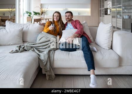 Una coppia di famiglie rilassata guarda la TV seduto su un comodo divano a casa e guarda le serie di film preferite Foto Stock