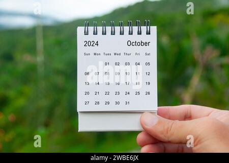 Mano che tiene il calendario bianco del 2024 ottobre con sfondo naturale. Concetto di calendario e festività. Foto Stock