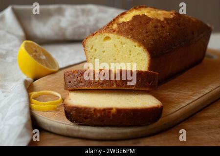 Deliziosa torta al limone fatta in casa con metà limone su un tagliere su uno sfondo di legno. Foto Stock