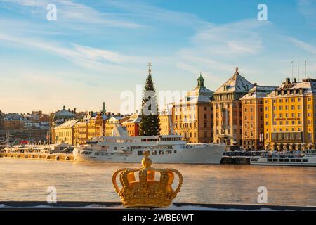 Il simbolo della corona reale svedese, sul ponte Skeppsholmen, che si affaccia sulla città vecchia e sull'albero di natale, in una fredda giornata invernale di sole, neve. Foto Stock