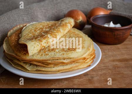 Crepes (lini russo) con cipolle e panna acida su sfondo di legno, vista dall'alto. Crepes fresche e sottili fatte in casa per colazione Foto Stock