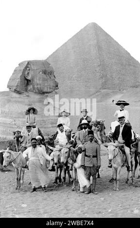 I turisti edoardiani posano con i cammelli e i loro autisti di fronte alla grande Piramide e alla Sfinge a Gaza, in Egitto. C1910 foto vintage o storica in bianco e nero o monocromatica Foto Stock