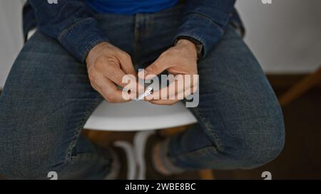 Bellissimo giovane ispanico che tiene tranquillamente la carta in mano seduto in sedia, assorbito dai pensieri, lo sfondo della sala d'attesa che crea un po' al chiuso Foto Stock