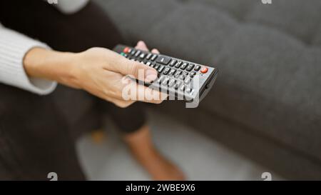 Un primo piano della mano di una donna con un telecomando televisivo, che ritrae il tempo libero a casa. Foto Stock