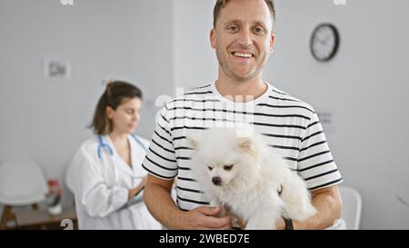 Felice giovane uomo caucasico in piedi con sicurezza con il suo cane sorridente nella vivace e vivace sala d'attesa di una clinica veterinaria di fiducia Foto Stock