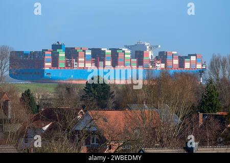 Enorme nave container sul fiume Elba passando per il villaggio di Altenbruch vicino Cuxhaven, Germania. Foto Stock